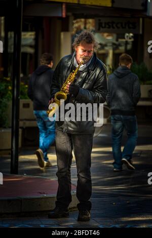 Launceston soulful solo performance by a leather jacket clad street saxophonist in dappled light. Stock Photo