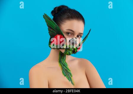 Woman with painted parrot bird on her face. Body art with real wings on the cheeks Stock Photo