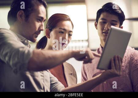 three young asian businessmen entrepreneurs working together in office looking at digital tablet Stock Photo