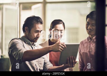 three young asian businessmen entrepreneurs working together in office looking at digital tablet Stock Photo