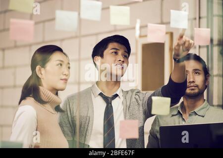 three asian small company businesspeople young entrepreneurs meeing discussing in office using sticky notes Stock Photo