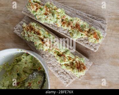 Top view on wooden table where located round container with guacamole and two piles of cereal chips topped with Mexican spread Stock Photo