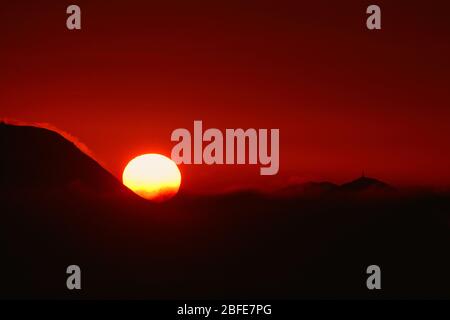 Big sun in a fiery red sunset on an island Stock Photo
