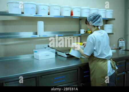 At the bakery: female baker putting flour with measuring spoon in a pan placed on a weigher Stock Photo