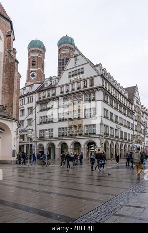Feb 2, 2020 - Munich, Germany: HIRMER House on street of Munchen with domed towers of Gotchic church Frauenkirche Stock Photo