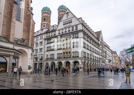 Feb 2, 2020 - Munich, Germany: HIRMER House on street of Munchen with domed towers of Gotchic church Frauenkirche Stock Photo