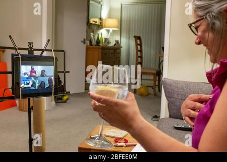 Middle aged woman sits in her home drinking alcohol, talking to friends via  video telecommunication Zoom during Coronavirus pandemic in UK Stock Photo