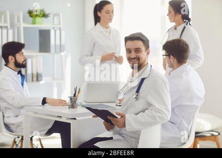 Male doctor sitting at a table with collegues in white lab coats at a medical hospital. Stock Photo