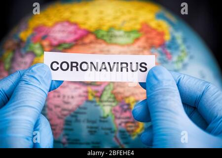 Person in medical gloves holding the word Coronavirus in his hands against a globe. Close up. Stock Photo