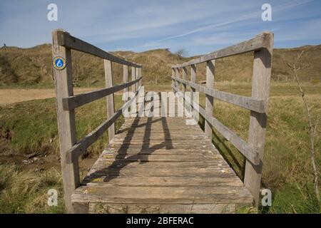 wooden footbridge taking Wales coast path over an inlet of the Ogmore river in Mertrhy Mawr nature reserve Stock Photo