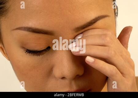 A young distressed woman holding her left hand over her left eye Stock Photo