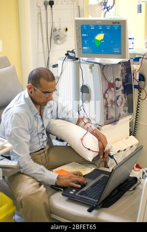 A business executive at work on his computer while being connected to a hemodialysis machine which is cleaning his blood of waste kidney fluids and to Stock Photo