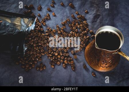 Flat lay of dark roast coffee beans scattered on dark background with turkish coffee pot, copper or cezve. Brewing traditional turkish coffee Stock Photo
