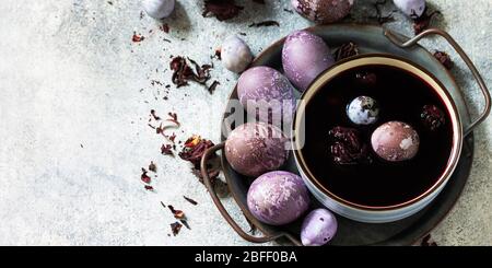 Natural egg dye purple. Easter eggs are painted with natural egg dye from Hibiscus tea on a gray stone countertop. Banner. Stock Photo