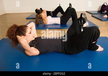 An exercise class at the Body Control Centre in London practice a Pilates Curl Up position using an inner thigh squeezing fitness ring.  Pilates is th Stock Photo