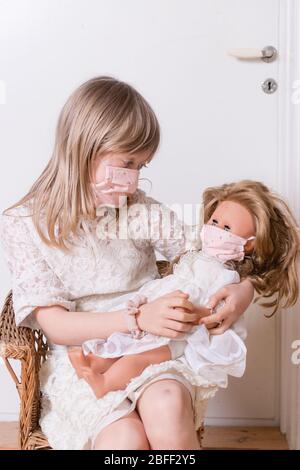 girl with homemade covid 19 protection mask with her doll Stock Photo