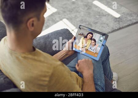 Family communicates online video call. Father talks with wife and daughter using tablet computer while sitting at home. Stock Photo