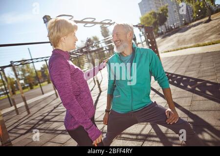 Happy and healthy. Smiling mature family couple in sportswear doing gymnastics together at outdoor gym. Man and woman doing stretching exercises Stock Photo