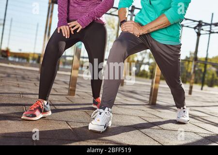 Stretching legs. Cropped photo of a couple in sportswear warming up together at the stadium. Man and woman doing stretching exercises outdoors Stock Photo