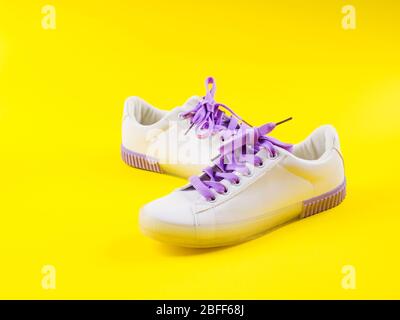 White sneakers with purple laces on yellow background Stock Photo