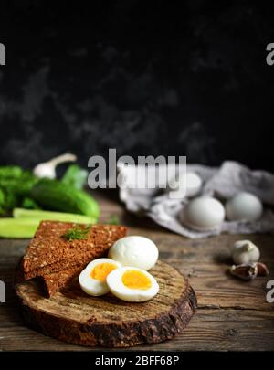 Boiled Chicken Eggs. Healthy breakfast in the village. Wood background. Dark photo. Free space for text. Cucumbers, wooden cutting board. Vertical vie Stock Photo