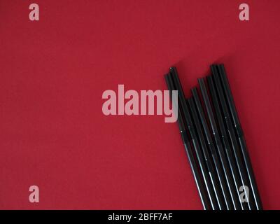 Black plastic single use straws isolated on red background. Top view. Stock Photo