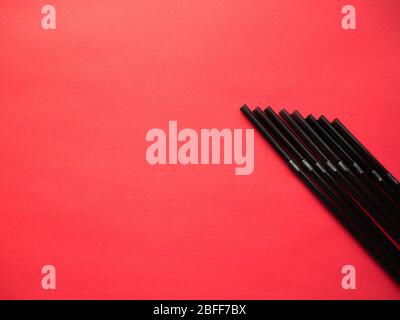 Black plastic single use straws isolated on red background. Top view. Stock Photo