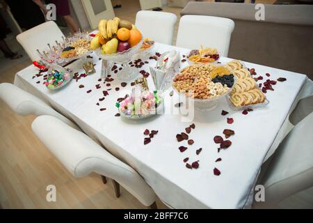 There are petals, walnut kernels, hazelnut kernels, raisins, almonds, fruits and candies on the table. An engagement table designed for engagement. Stock Photo
