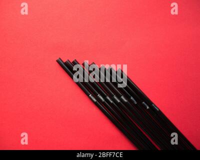 Black plastic single use straws isolated on red background. Top view. Stock Photo