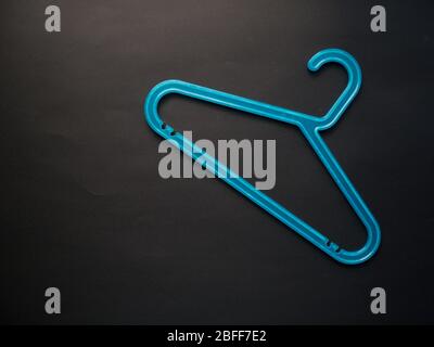 Blue plastic hanger on pastel black background. Shopping, sale, promo, social media, new season concept. Top view. Stock Photo