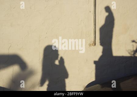 Shadow of a little girl praying to the statue of the Madonna at sunset Stock Photo