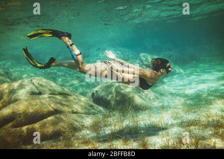 A beautiful young woman is having fun at summer vacation exploring seafloor during scuba diving in sea. Stock Photo