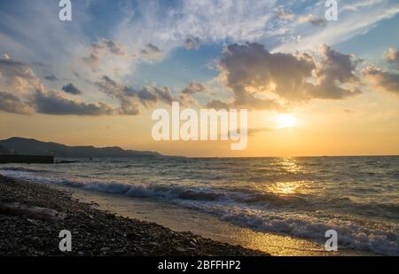 Amazing sea sunset on the pebble beach, the sun, waves, clouds Stock Photo