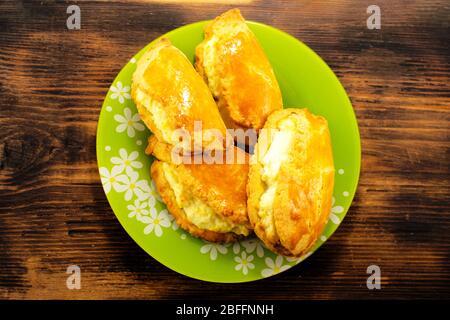Tasty and lush homemade buns stuffed with cottage cheese on a green plate and wooden background. Stock Photo