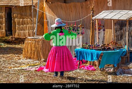 Indigenous art and craft saleswoman in flashy tribal colors on the Uros floating Islands with totora reed houses and floor, Titicaca Lake, Peru. Stock Photo