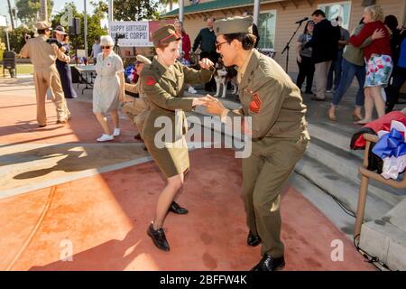 Dressed as U.S. Marines, a couple enthusiastically dances a World War II-style jitterbug at Veterans Day observances in Costa Mesa, CA. In background is a woman in a Red Cross 'girl' uniform. Stock Photo