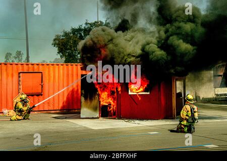 Firemen spray water on a burning model living room in a fire department structural firefighting demonstration in Costa Mesa, CA. Stock Photo
