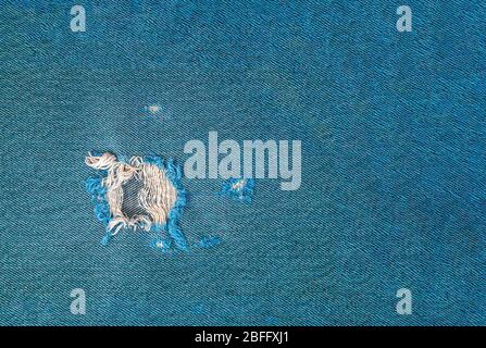 close up of frayed hole in turquoise denim fabric Stock Photo