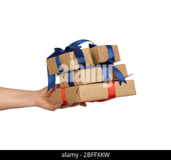 hand holds a stack of wrapped gifts in brown craft paper with tied silk bows, subject is isolated on a white background Stock Photo