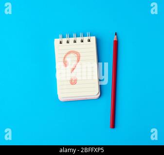 notebook in line and wooden red pencil on a blue background, drawn question mark on a white sheet Stock Photo