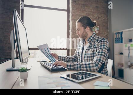 Photo of business finance administrator guy computer monitor table look check graphics charts on paper compare with online numbers wear casual shirt Stock Photo