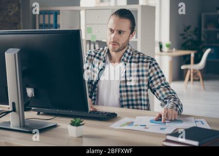 Photo of business finance administrator guy computer table look check graphics charts on paper compare with online numbers stats wear casual shirt sit Stock Photo