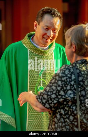 A robed Vietnamese American priest chats with a parishioner after mass at a Southern California Catholic church. Stock Photo