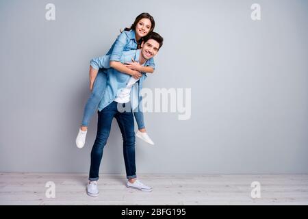 Full length photo of positive passionate spouses enjoy summer honeymoon rest relax hug piggyback wear casual style outfit sneakers isolated over gray Stock Photo