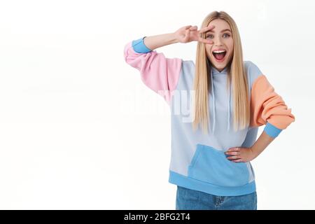 Happiness, big announcement and lifestyle concept. Cheerful happy blonde girl in hoodie, showing peace sign over eye, smiling kawaii, enjoying Stock Photo