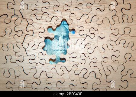 Benjamin Franklin on the $100 bill peeks through an unfinished jigsaw puzzle.