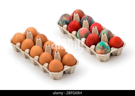 Packs of regular eggs and Colorful Easter eggs in cardboard egg box on white background. Raw chicken eggs in open egg box on a white background Stock Photo