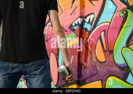 Young graffiti artist with backpack and gas mask on his neck paints colorful graffiti in pink tones on brick wall. Street art and contemporary paintin Stock Photo