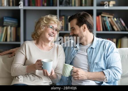Elderly mother and adult son drinking tea enjoy warm conversation Stock Photo
