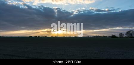 Panoramic view of the sun shining from behind a cloud bank. Divergent pattern of sun rays (crepuscular rays) over the wide open landscape of Holland. Stock Photo